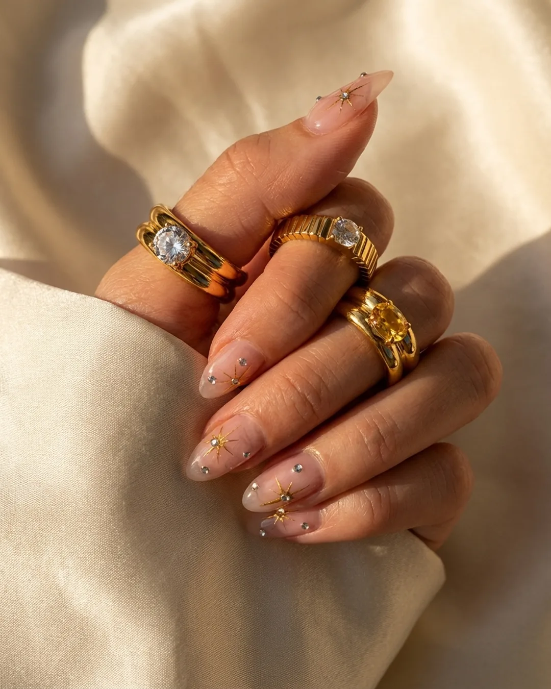Gold rings worn on a hand against cream silk